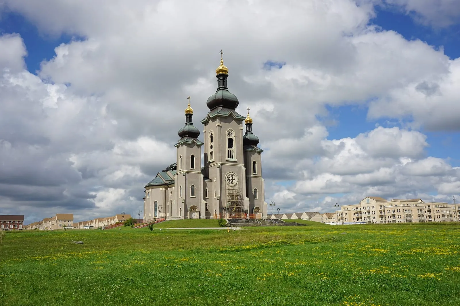 The Cathedral of the Transfiguration rising above an open field in Cathedraltown, Markham, with low-rise buildings in the distance.